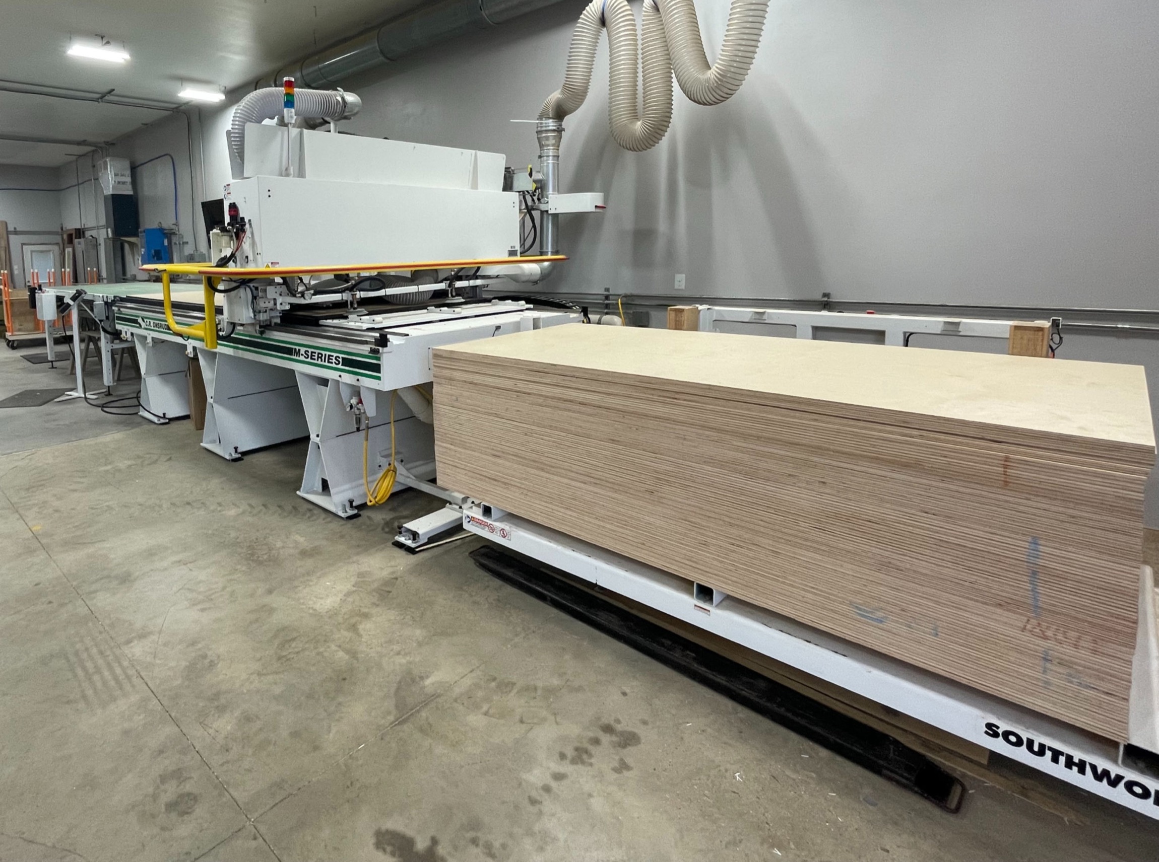 Industrial CNC woodworking machine with stacked plywood sheets in a workshop.