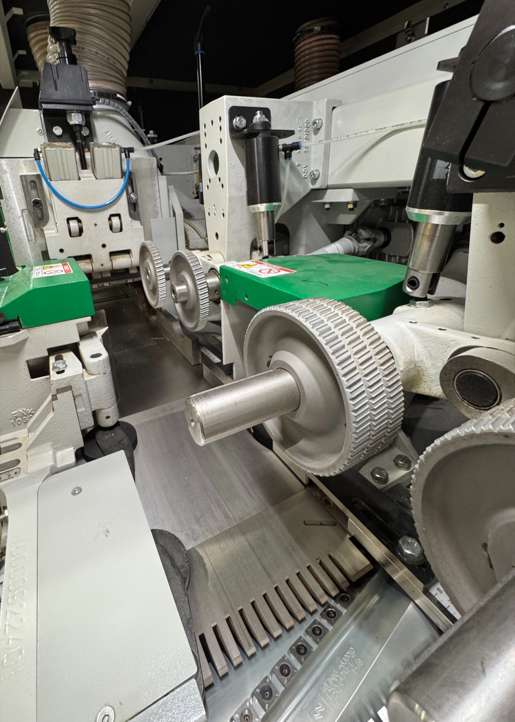 Industrial woodworking machine interior with green feed rollers and metal cylindrical components.
