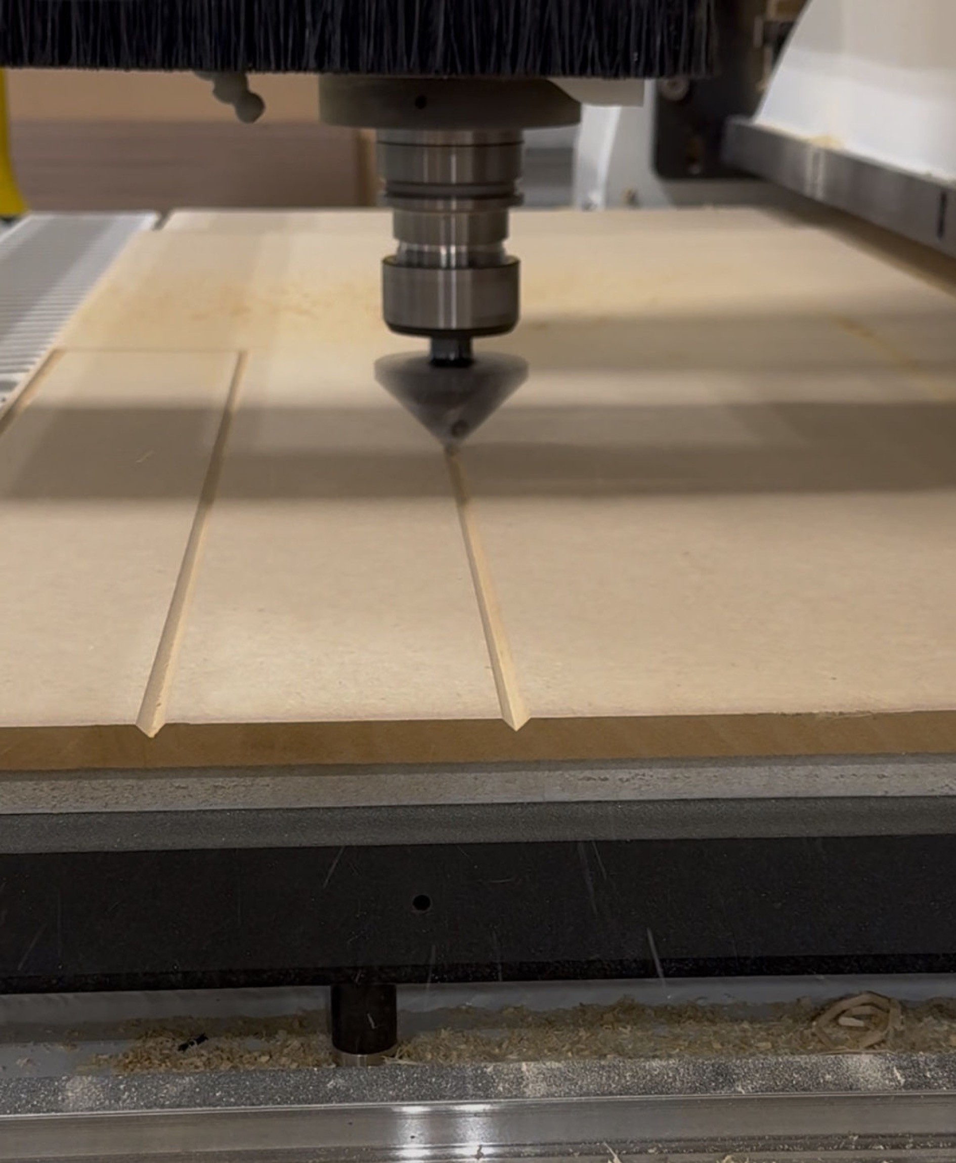 CNC machine spindle cutting grooves into a flat wooden board.