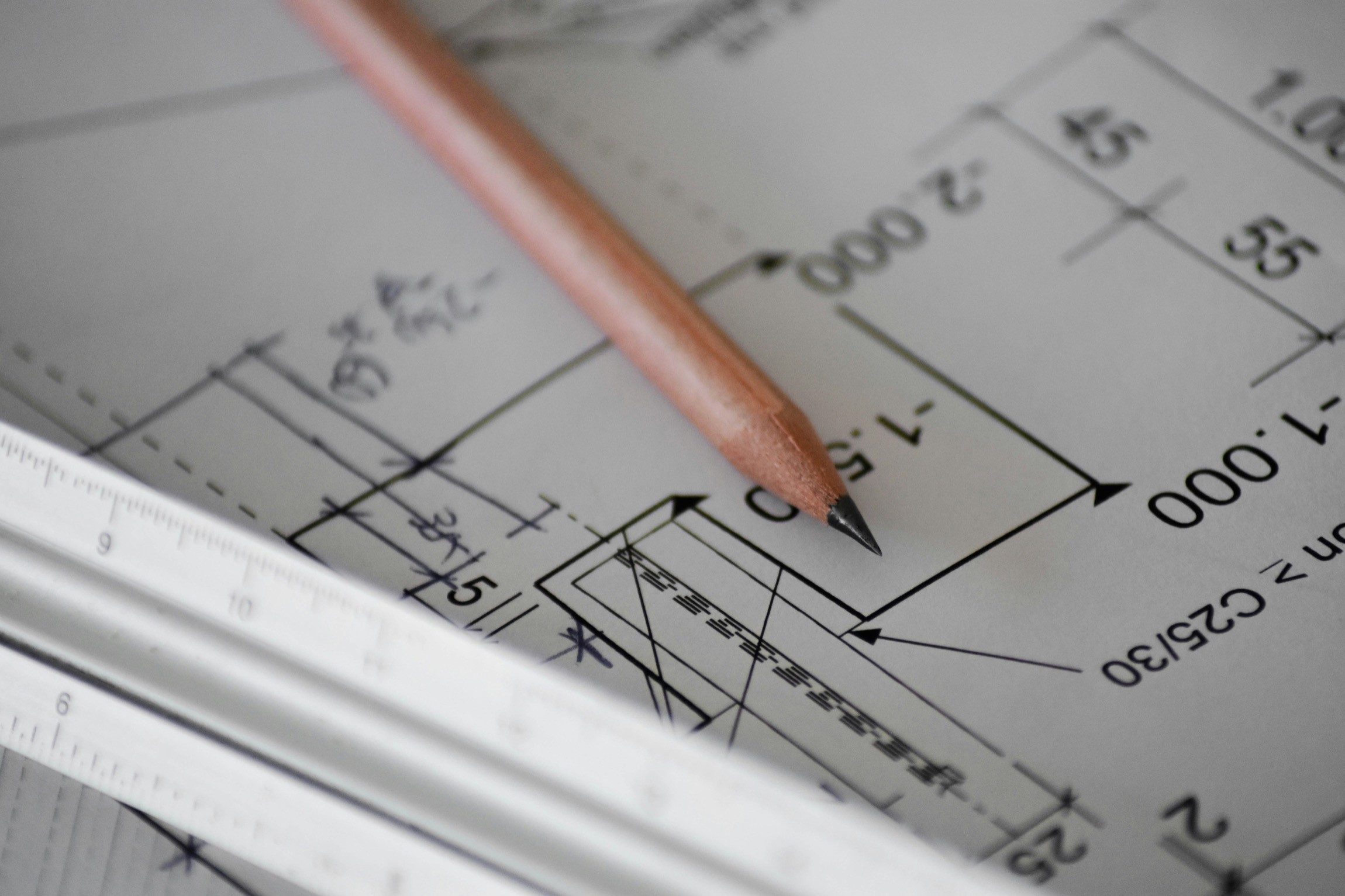 Pencil resting on architectural blueprint with dimensions, beside a metal ruler.