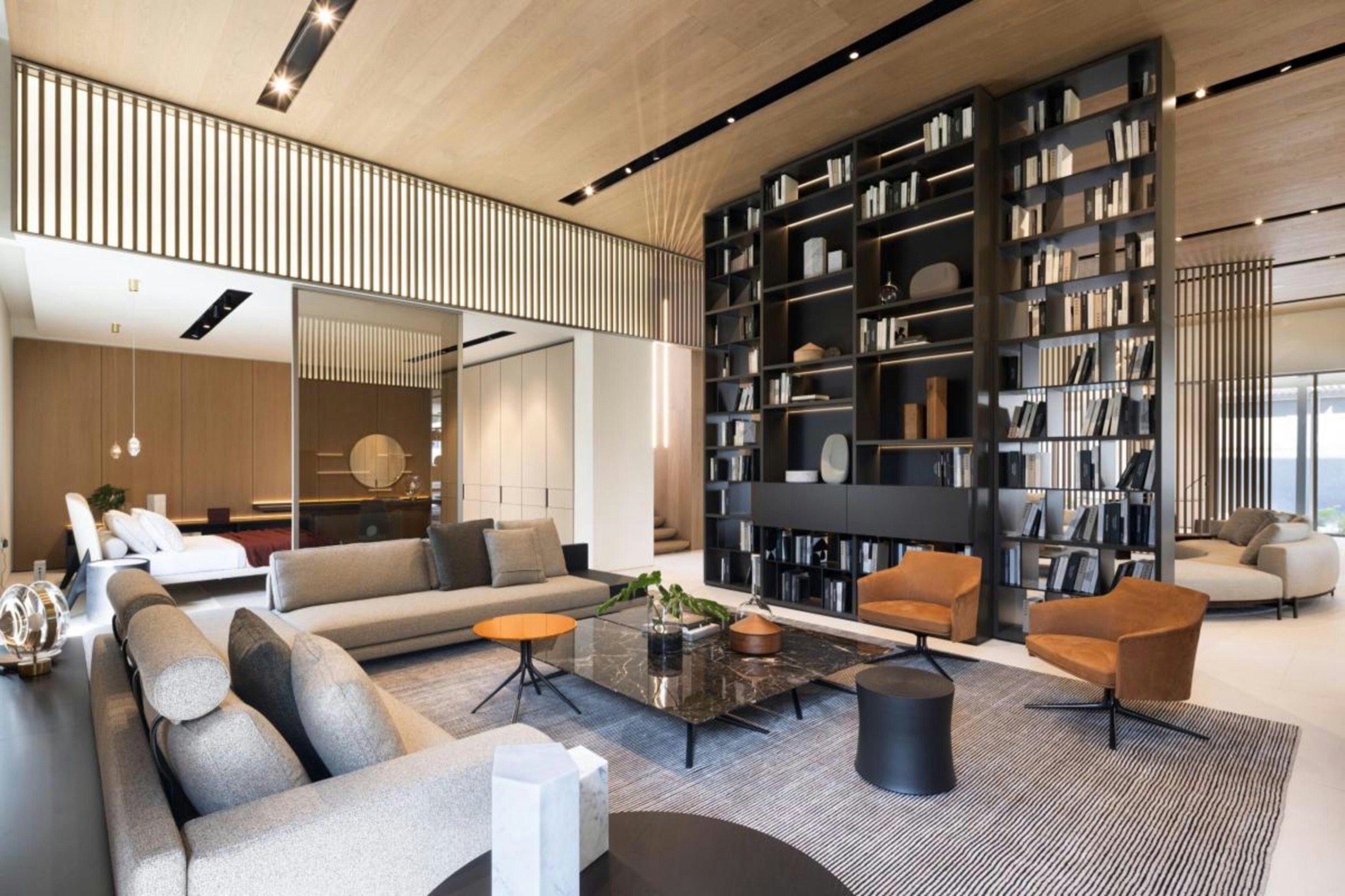 Modern living room with sectional sofa, tall dark bookshelves, leather armchairs, and wood-paneled walls and ceiling.