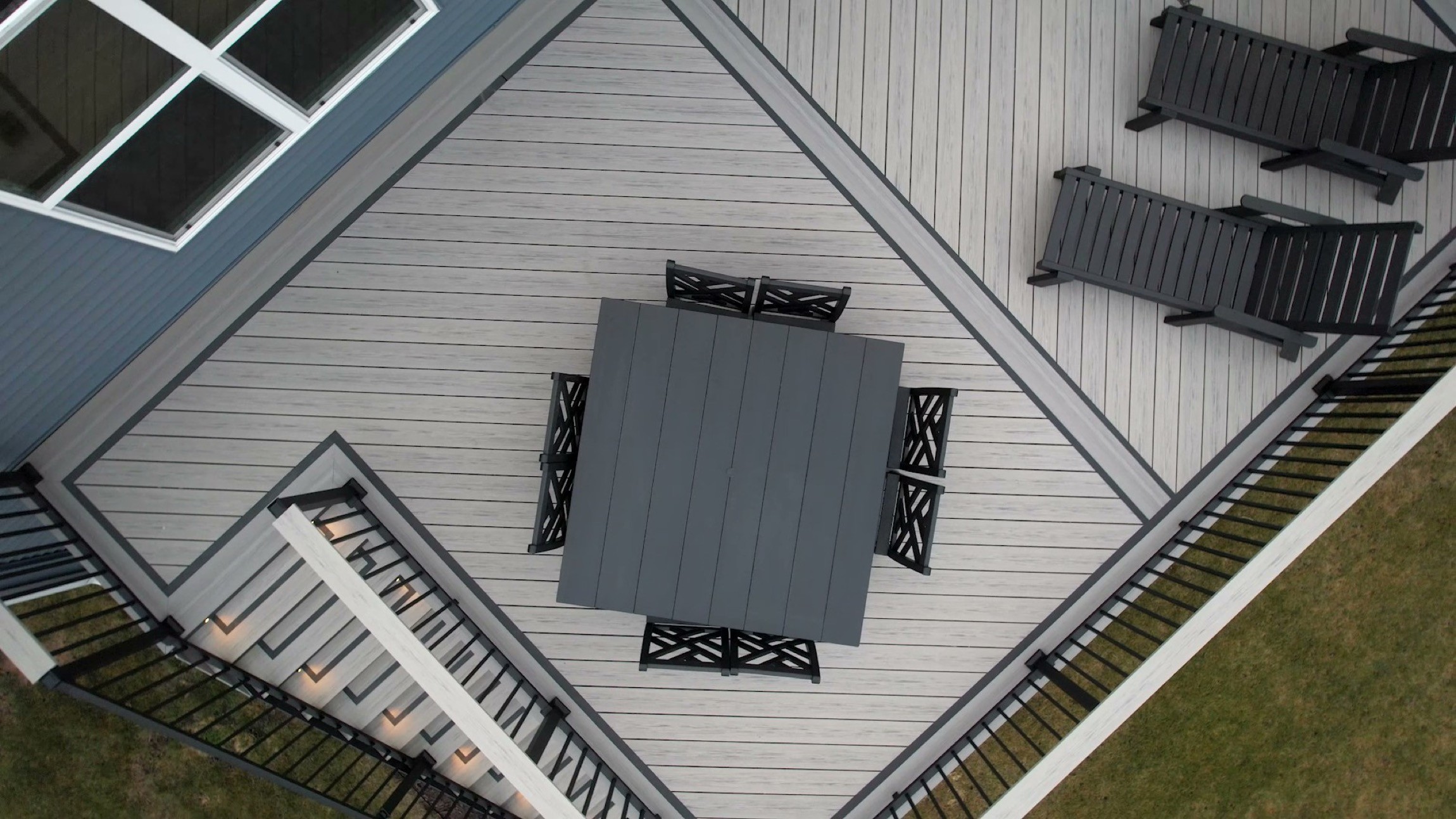 Aerial view of a gray composite deck with diagonal boards, black benches, and stairs.