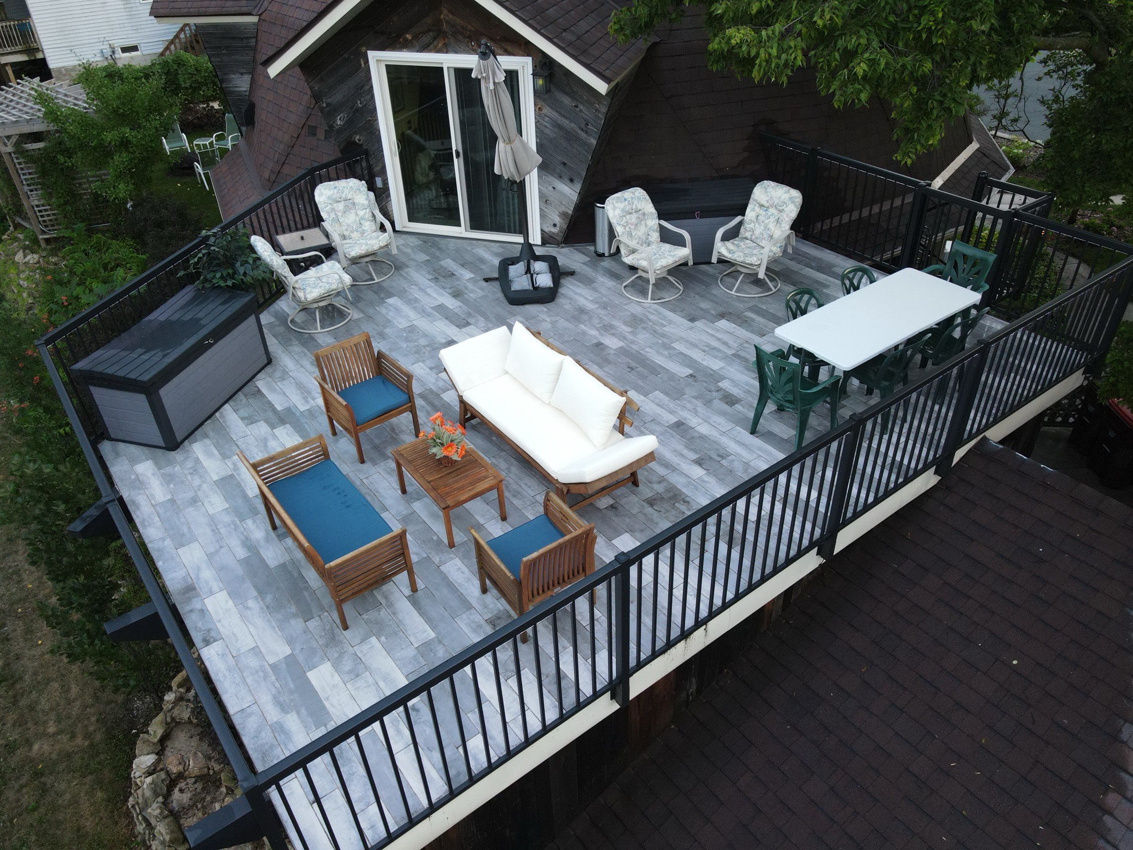 Aerial view of a gray tiled rooftop deck with patio furniture, dining set, and black metal railings.