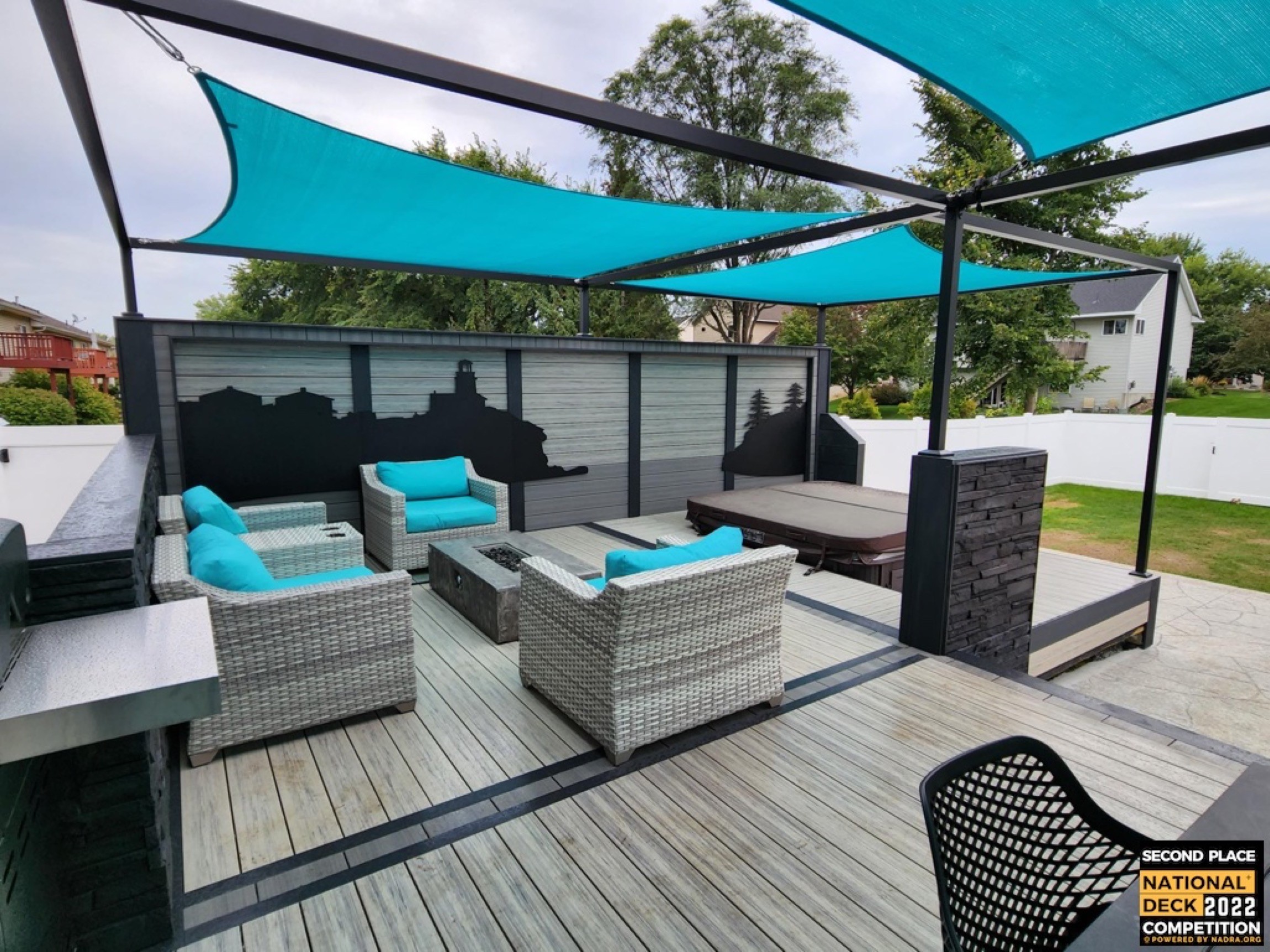Outdoor patio with gray wicker furniture, teal cushions, and turquoise shade sails over a wooden deck.