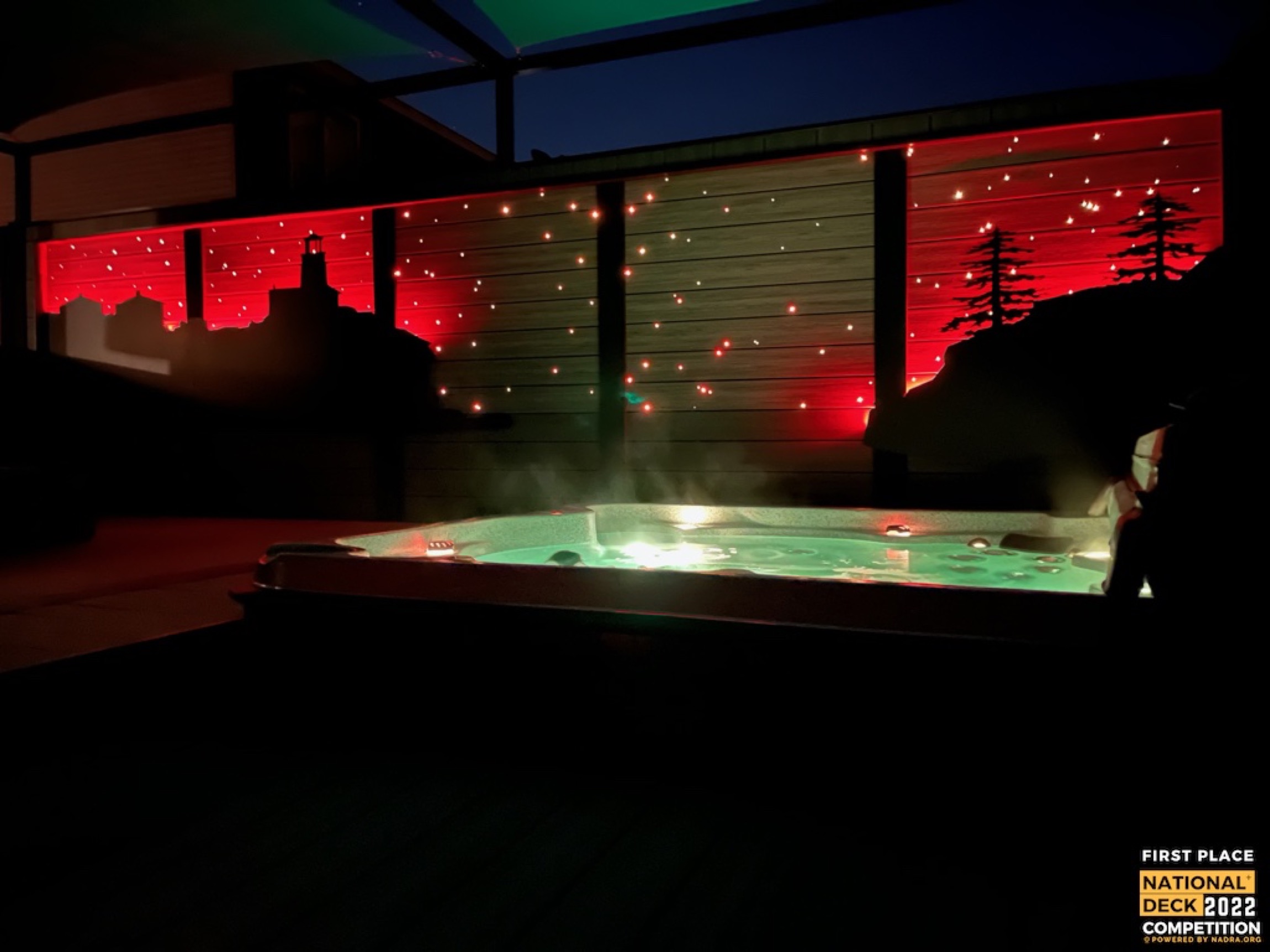 Illuminated outdoor hot tub at night with red-lit privacy walls and string lights overhead