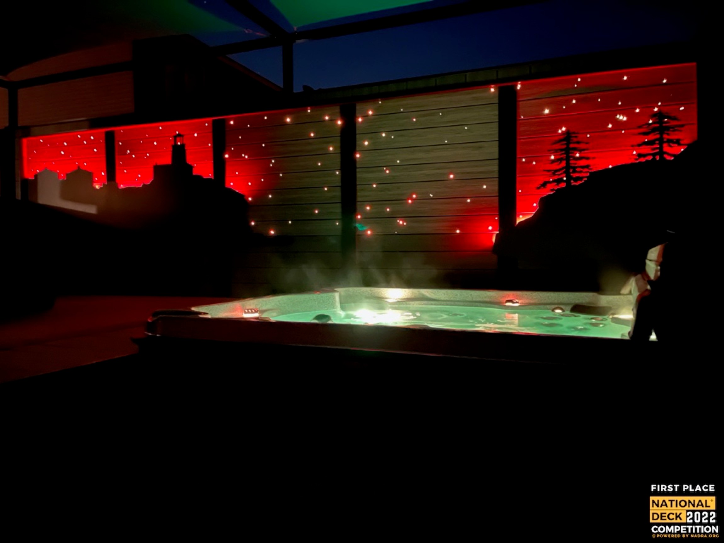 Illuminated outdoor hot tub at night with red-lit privacy walls and string lights overhead